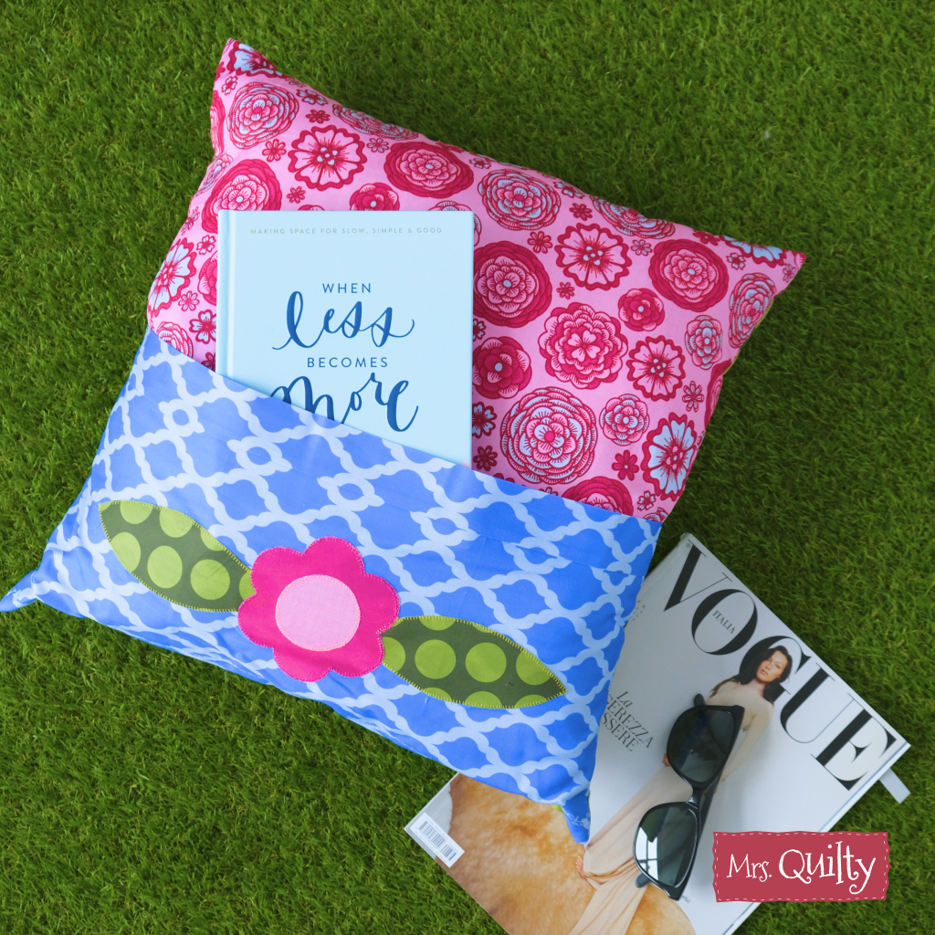 Two pillows made with the Reading Pillow Downloadable PDF Quilt Pattern, featuring floral designs, a copy of "When Less Becomes More," a Vogue magazine, and sunglasses are displayed on green grass.