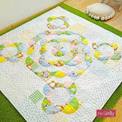 A vibrant quilt with circular animal and geometric patterns adorns the wooden floor, accompanied by a green rug and round cushion, enhancing festive home decor. Discover more with our Spring Magazine – 8 Quilting Patterns Inside! Downloadable PDF.