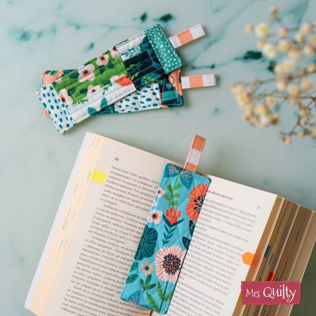 A PDF quilt pattern for making fabric bookmarks is featured clipped to an open book, with additional handmade bookmarks displayed nearby on a marble surface.