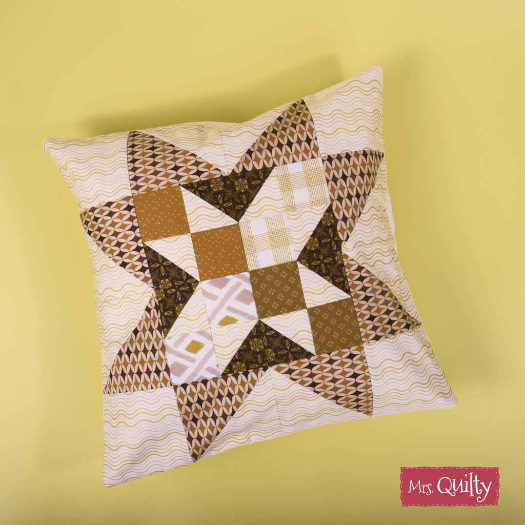 The Decorative Cushion Cover Downloadable PDF Quilt Pattern features a brown and cream geometric star on yellow, with a "Mrs. Quilty" logo in the corner. Includes an easy-to-follow digital quilting pattern for crafting your own cushion cover.