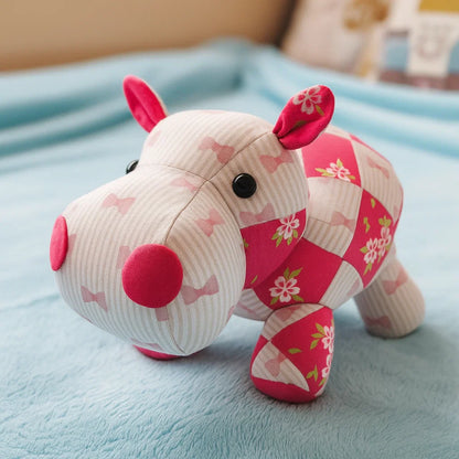 The Hilda the Hippo Downloadable PDF Quilt Pattern lets you create a charming hippo quilt with pink, white, and floral patchwork—reminiscent of a cute plush hippo resting on a light blue blanket.