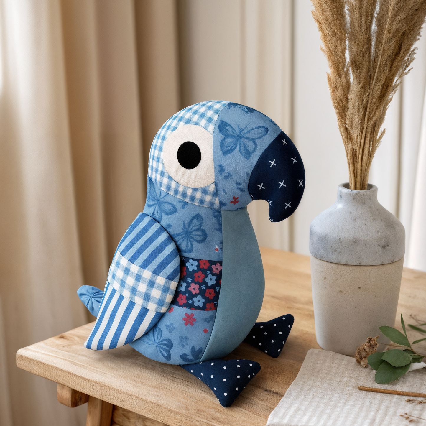 The Pip the Parrot Downloadable PDF Quilt Pattern is displayed on a wooden table next to a white vase of dried grasses.