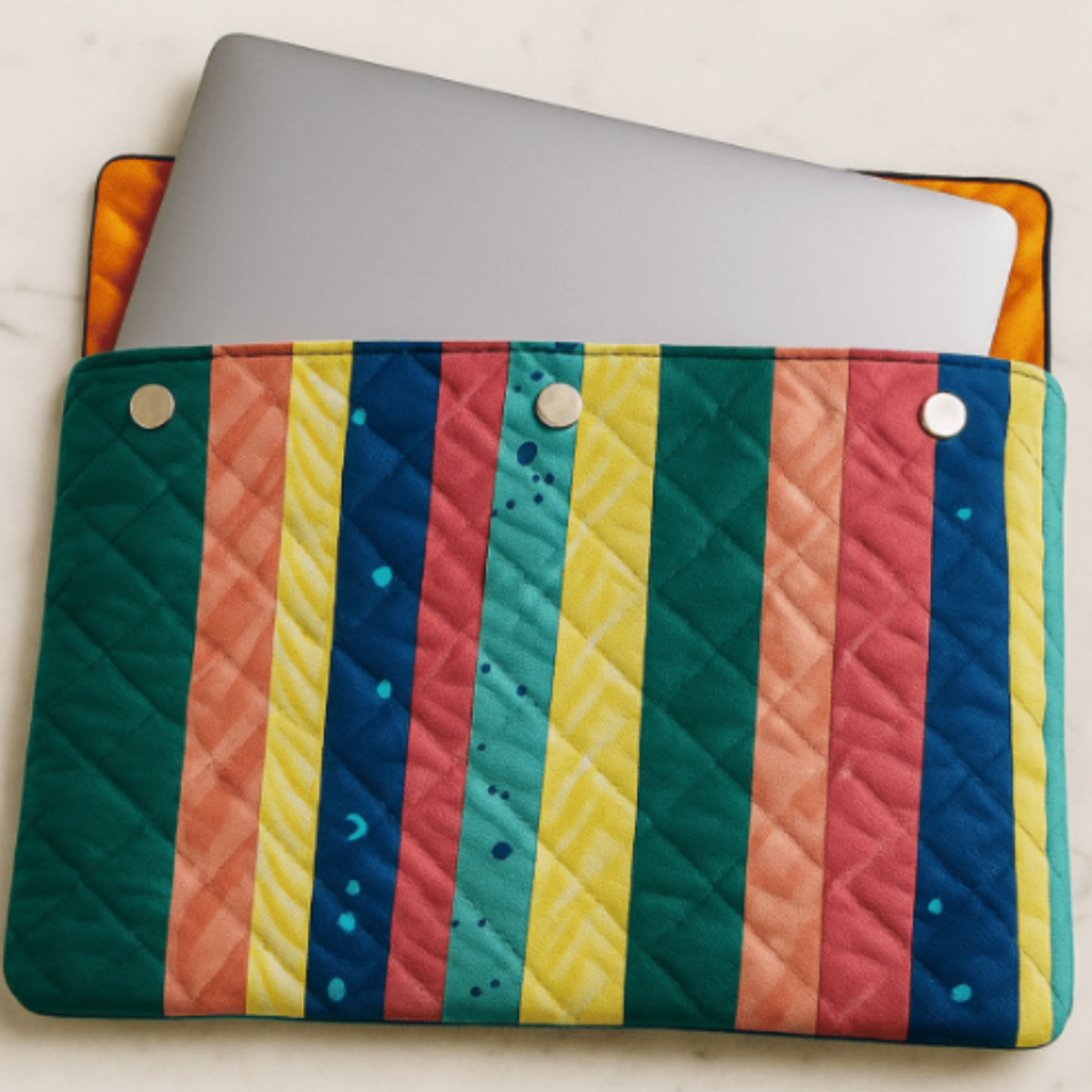 A laptop is partially inserted into the Stylish Quilted Laptop Sleeve, featuring a geometric patchwork design and three snap buttons, made using the downloadable PDF quilt pattern, displayed on a light surface.
